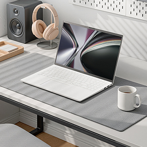 깨끗하고 밝은 화이트 톤의 책상 위에 화이트 색상의 노트북이 비스듬하게 열려 있습니다. 노트북 화면에는 회색의 부드러운 곡선이 겹쳐진 추상적인 배경화면이 나타나 있습니다.