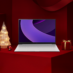 레드 기프트 박스 배경 위에 LG 그램 노트북이 놓여 있고, 좌측에는 조명 트리, 우측에는 리본이 묶인 선물이 배치된 연말 분위기의 구성.